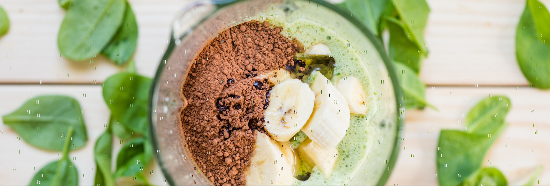 Imagem do alto de um copo de liquidificador com bananas, cacau em pó e leite
