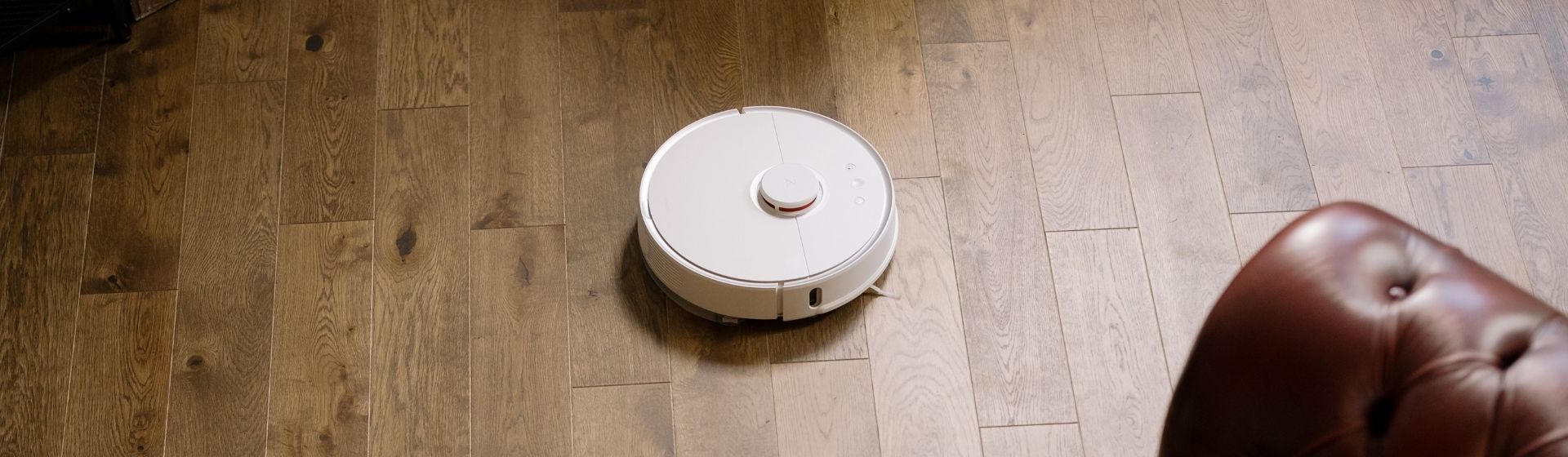 Aspirador de pó robô branco, redondo, no chão de madeira