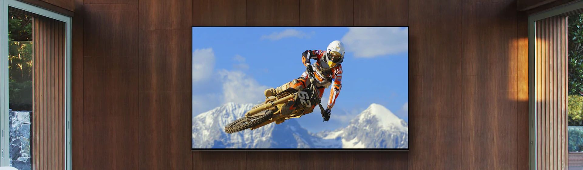 Smart TV plana em parede de madeira exibindo imagem de motocross