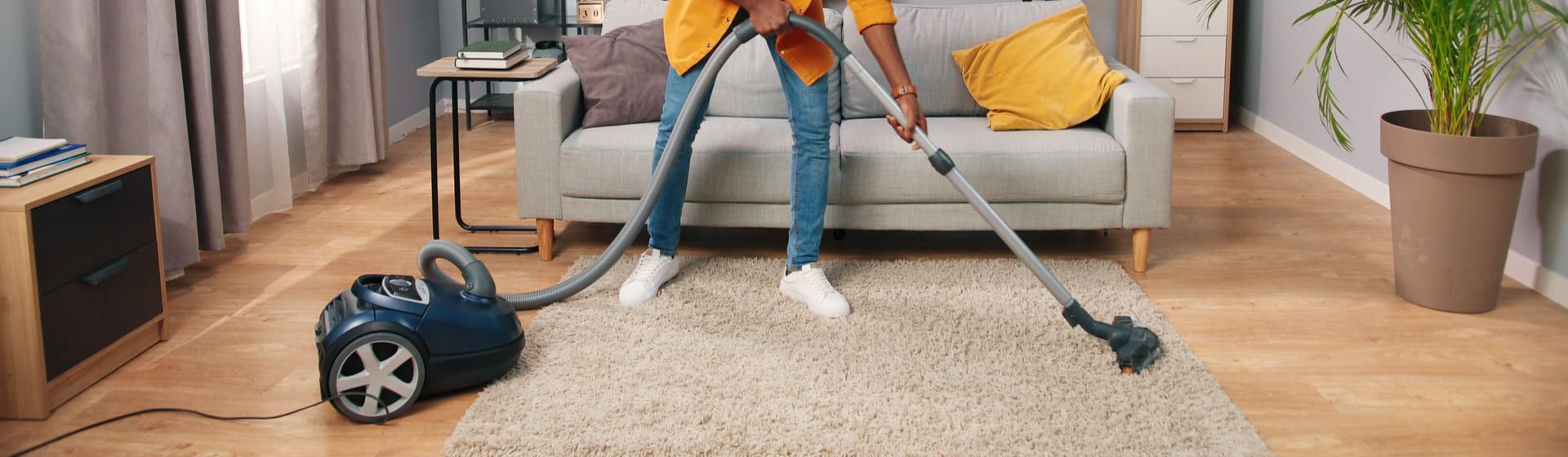 Homem negro usando um aspirador de pó para aspirar tapete numa sala de estar