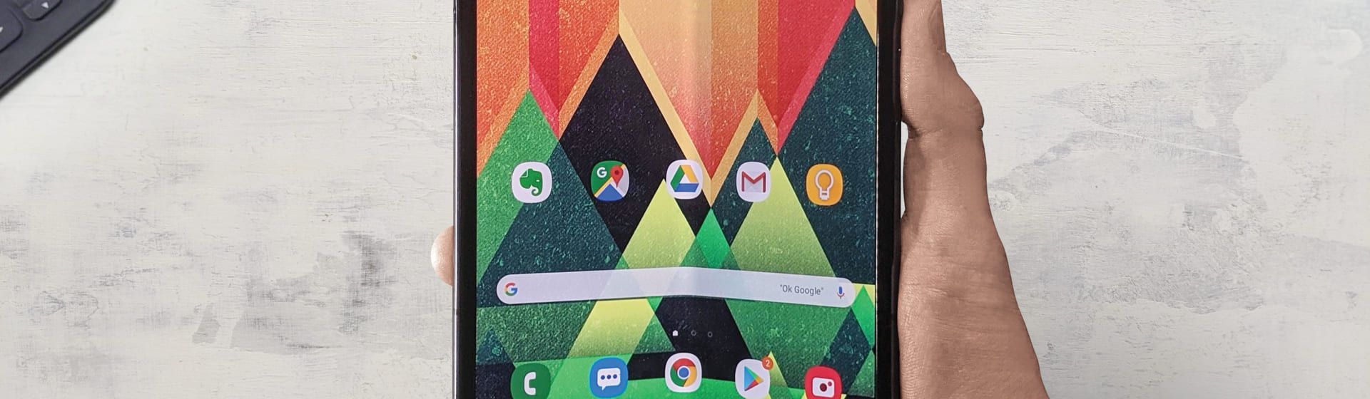 Celular que dobra sendo segurado por mão masculina com a tela ligada e fundo cinza