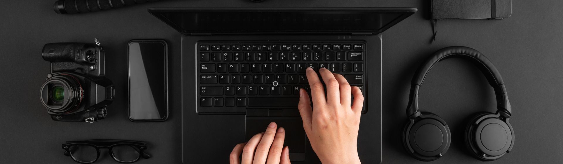 Notebook preto sobre mesa da mesma cor com câmeras e headsets em volta