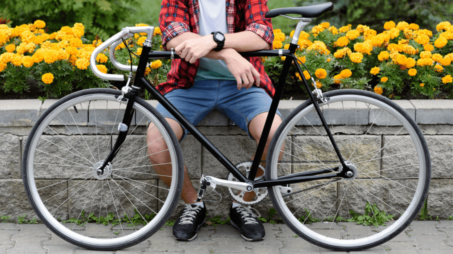 Close em pernas de homem sentado em mureta com uma bicicleta preta à frente