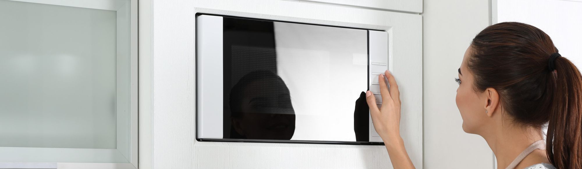 Mulher manuseando micro-ondas de embutir com porta espelhada instalado numa parede branca 