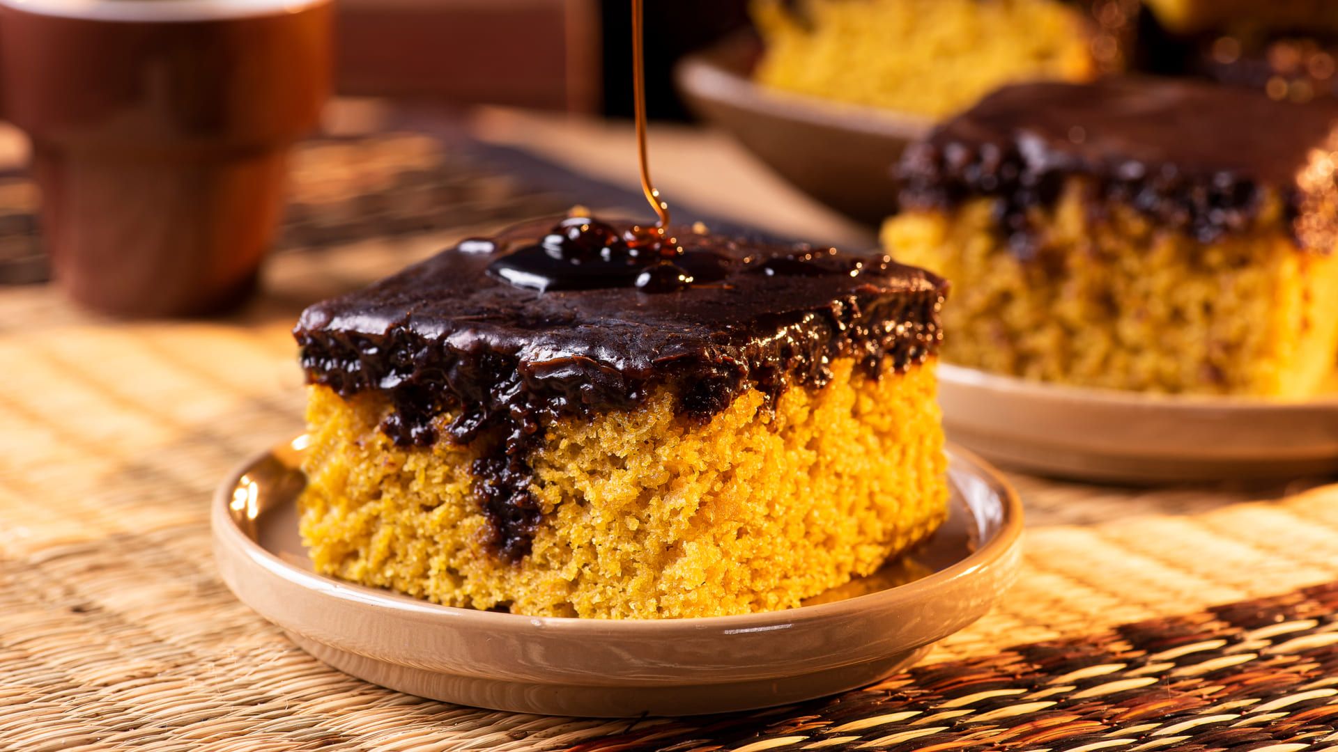 Pedaço de bolo de cenoura com calda de chocolate em um prato em cima da mesa.