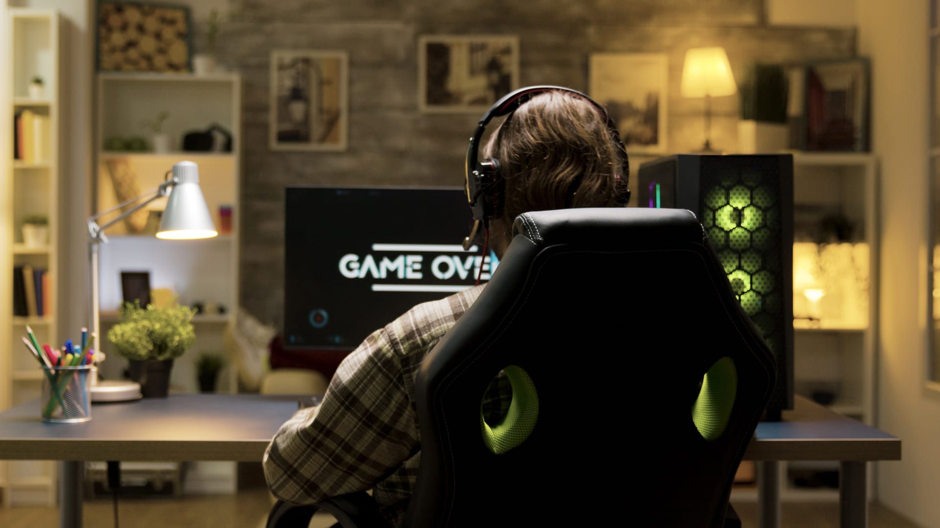 Jovem sentado em cadeira gamer jogando de frente para o computador e de costas para a foto.