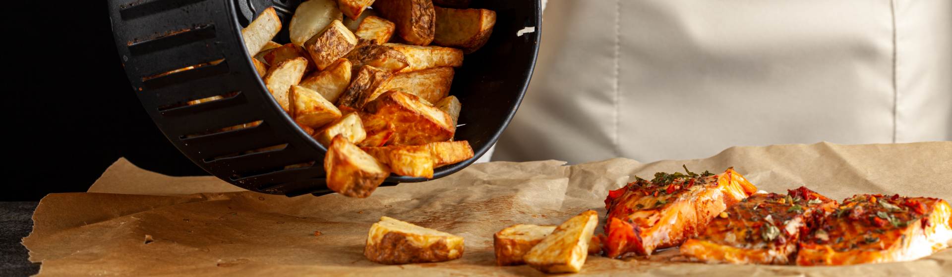 Batatas fritas preparadas na airfryer sendo colocadas numa bancada ao lado de filés de peixe grelhados