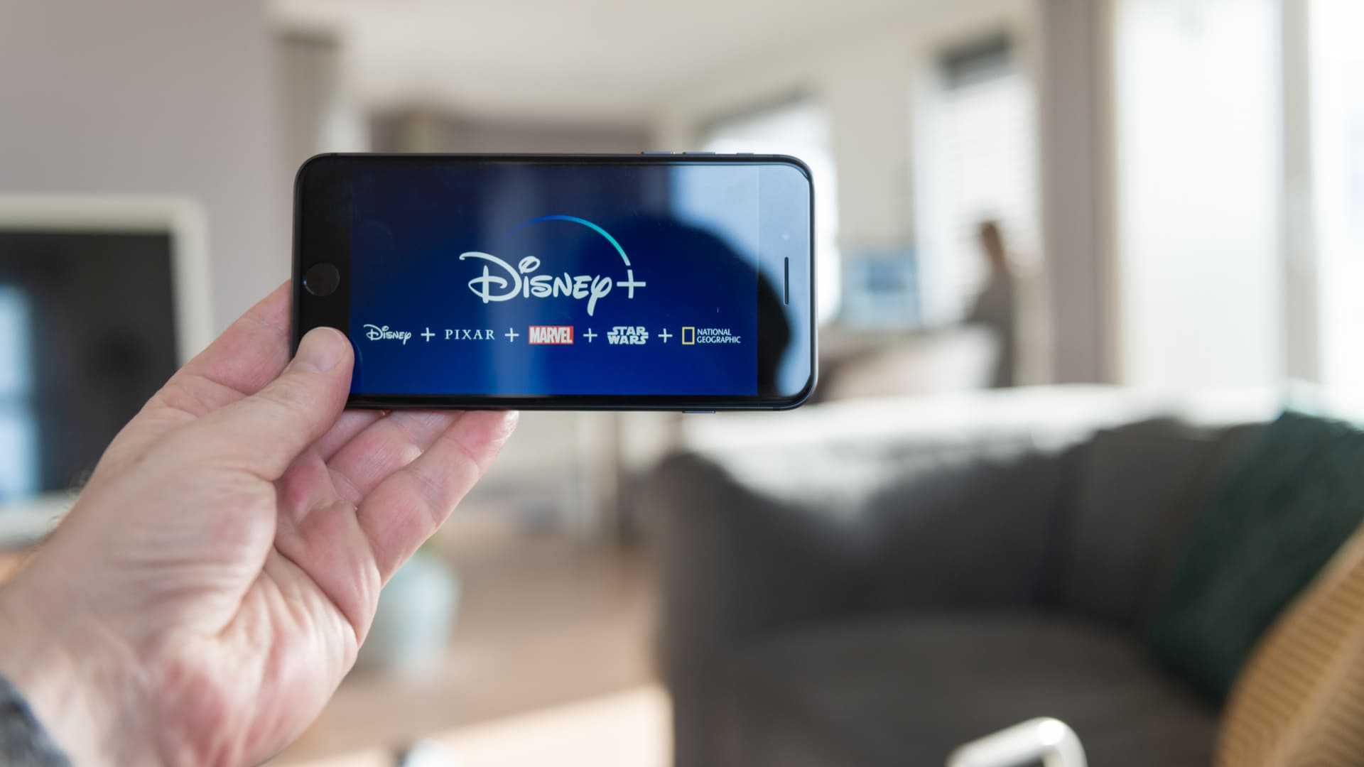 Disney Plus aberto na tela de um celular, segurado na horizontal por uma mão.