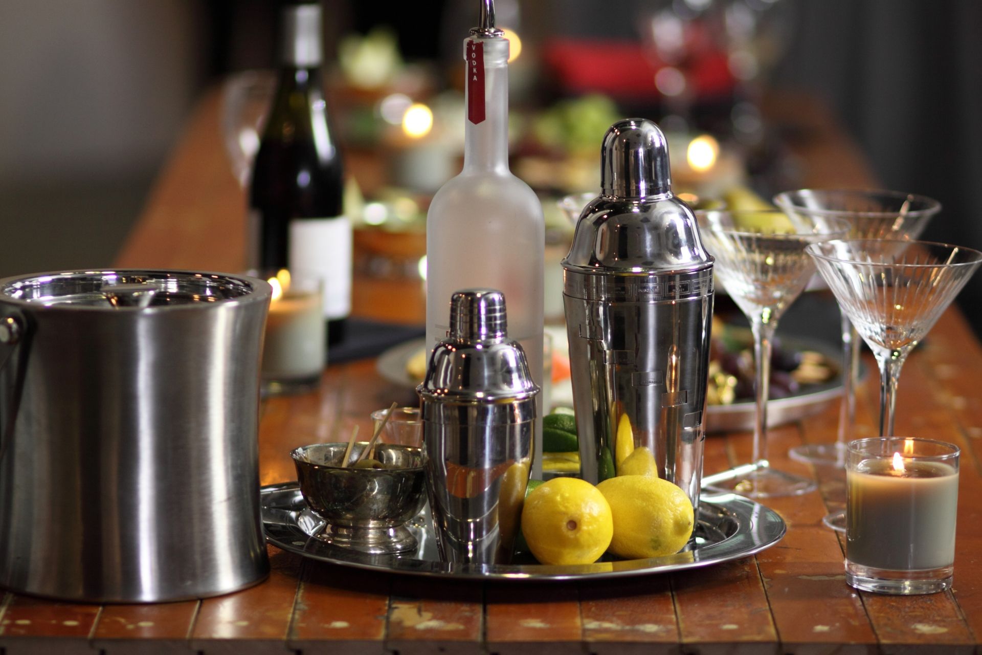 Mesa de madeira com coqueteleiras em cima de uma bandeja prata junto com um balde de gelo e três taças de martini