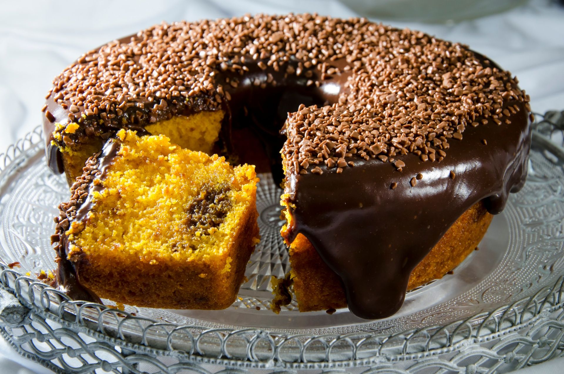 Bolo de cenoura com calda de chocolate e granulados por cima e fatia cortada