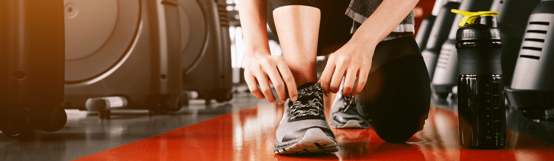 Mulher amarrando tênis para academia antes do treino com uma garrafa ao lado