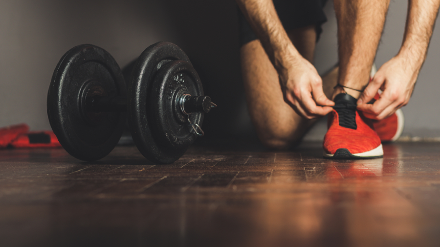 Homem amarrando tênis para academia antes do treino com um peso ao lado