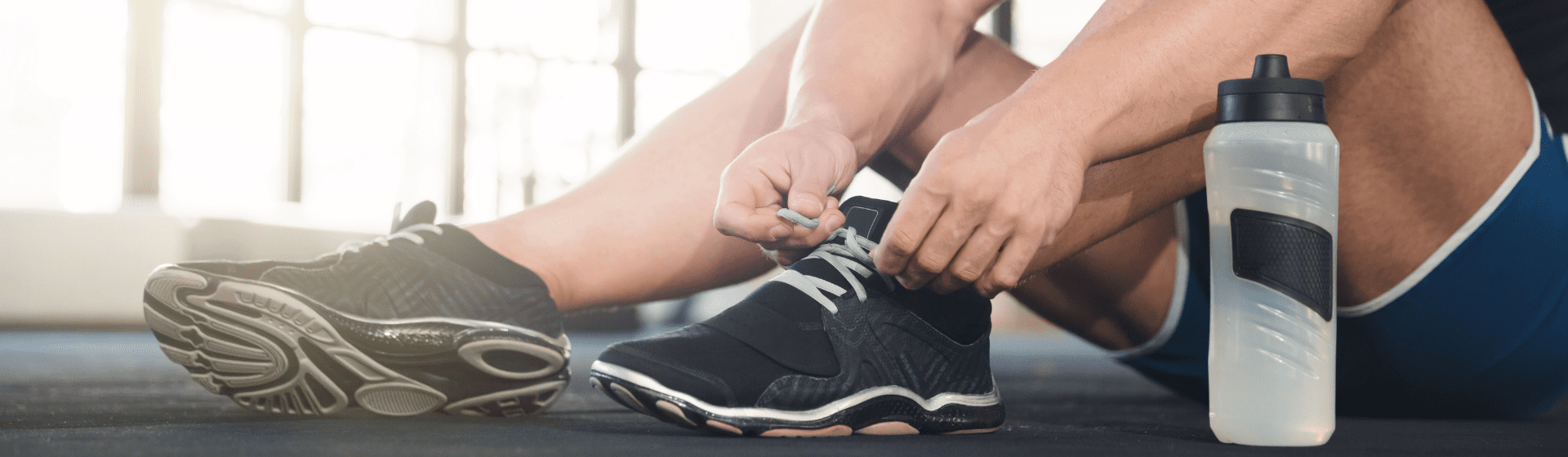 Homem amarrando tênis para academia antes do treino com uma garrafa ao lado