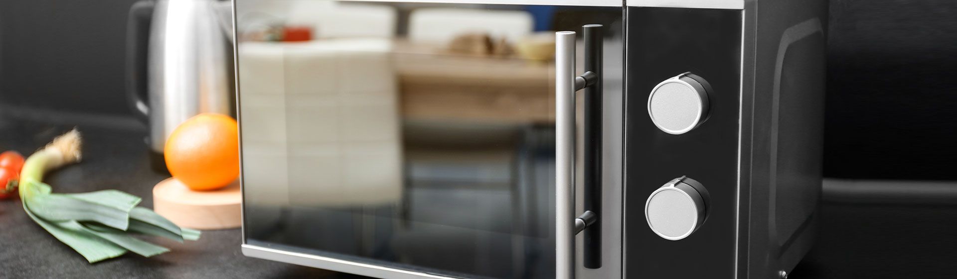 Micro-ondas com porta espelhada numa bancada de preta. Modelo é de inox e tem dois botões giratórios na lateral