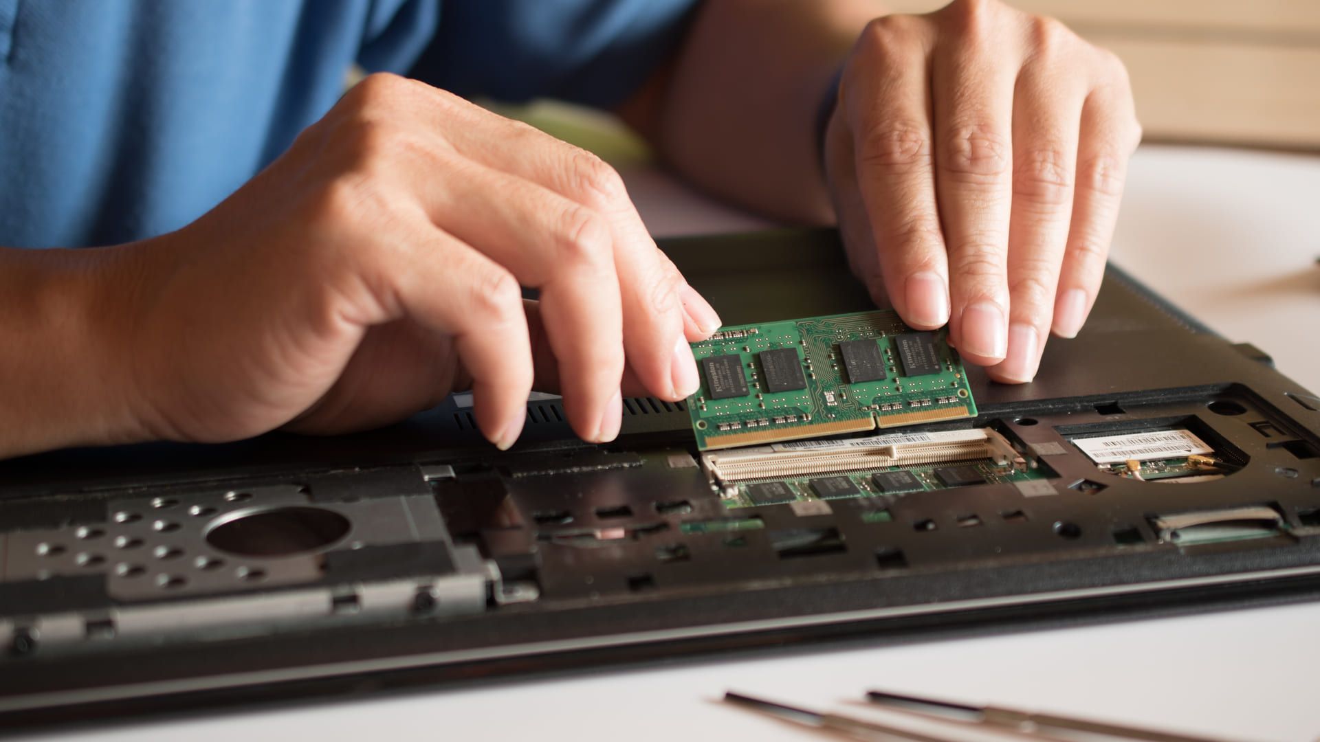 Parte de trás de um notebook com SSD sendo desmontada por duas mãos.