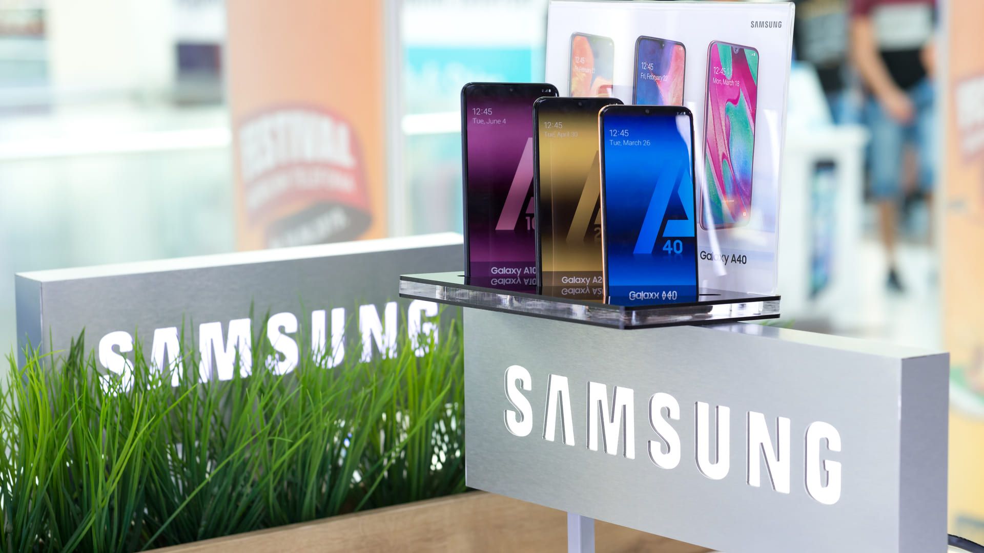 Três celulares samsung dispostos em prateleira acima do símbolo da marca