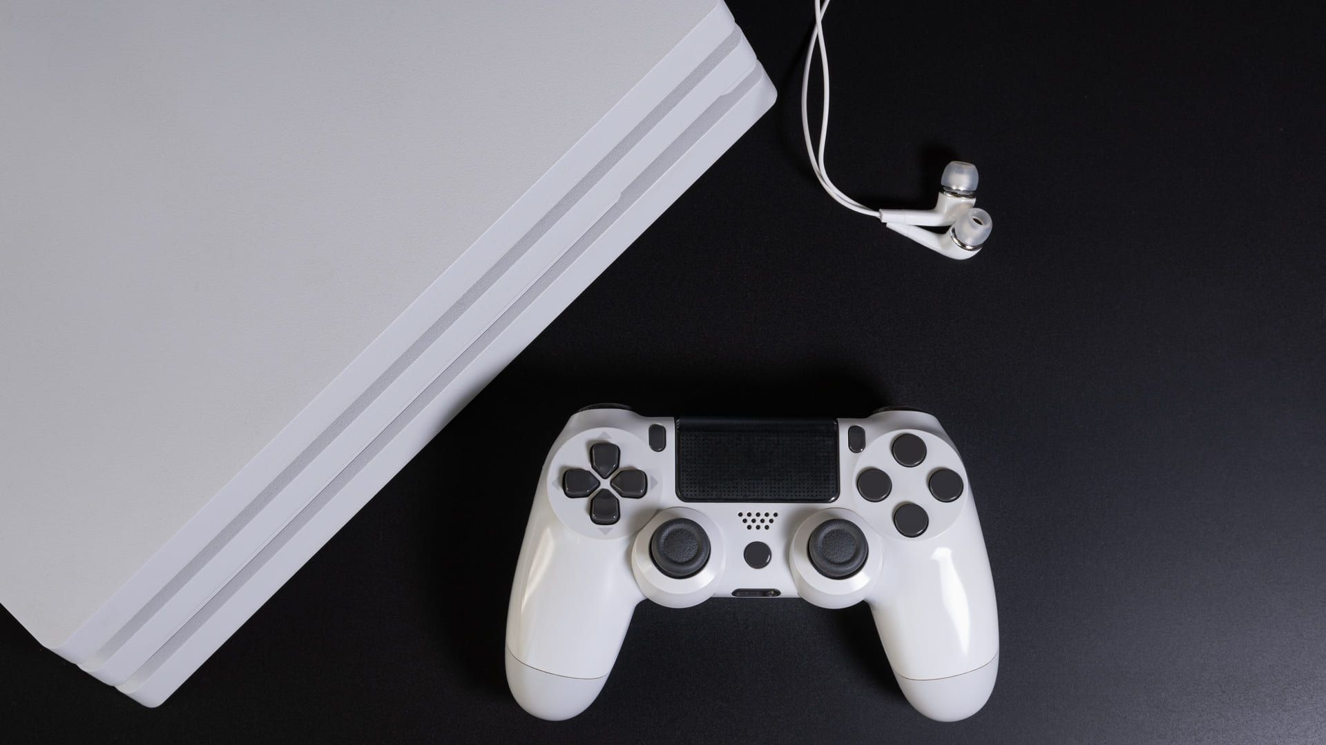 PS4 e controle branco sobre mesa preta, com fones de ouvido ao lado
