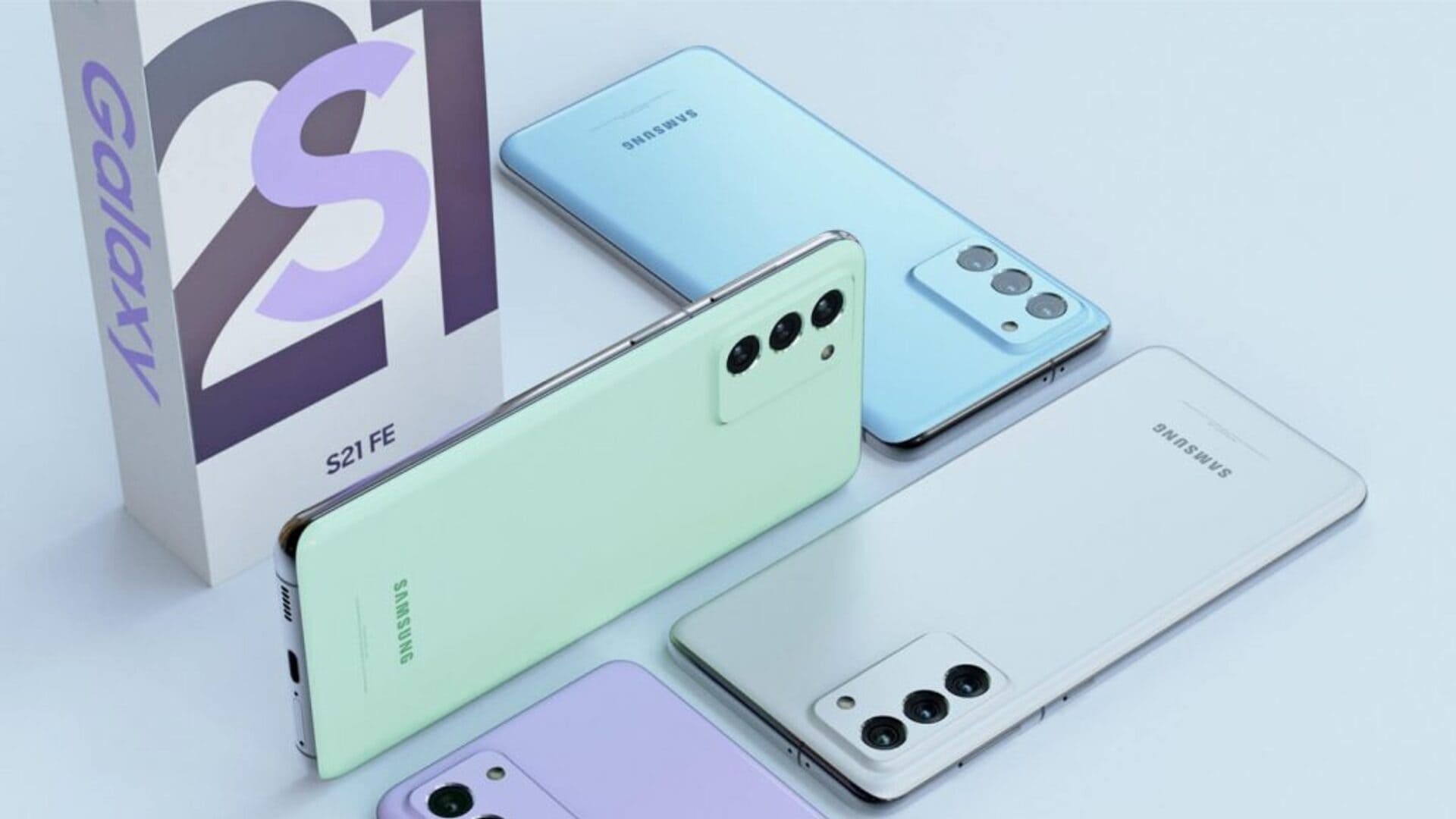 Quatro celulares Galaxy S21 FE de cores diferentes e caixa branca em fundo azul claro