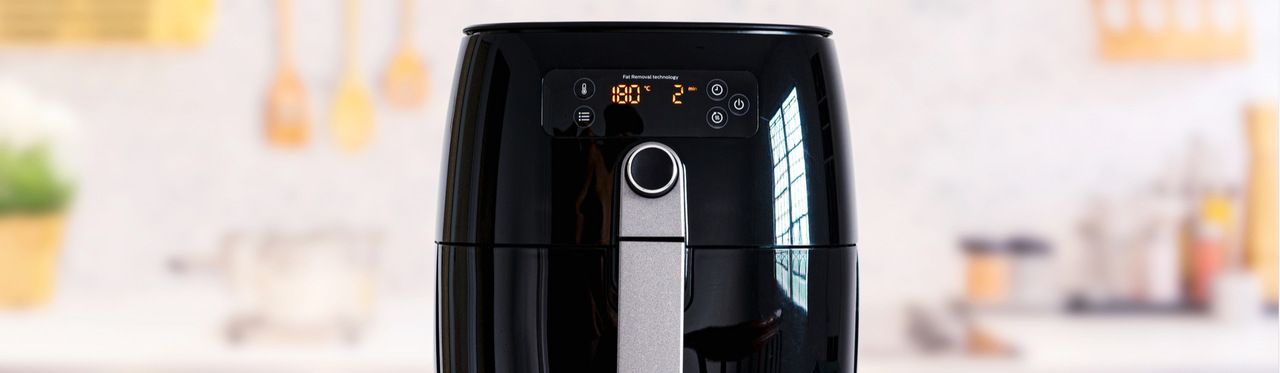 Air fryer digital preta sobre bancada em fundo desfocado.