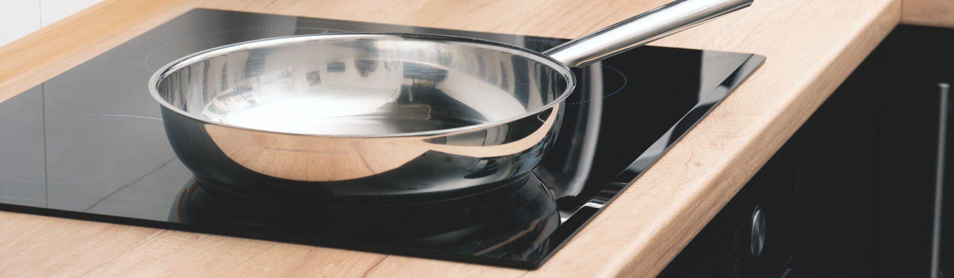 Frigideira de inox em um cooktop de indução preto instalado numa bancada de madeira