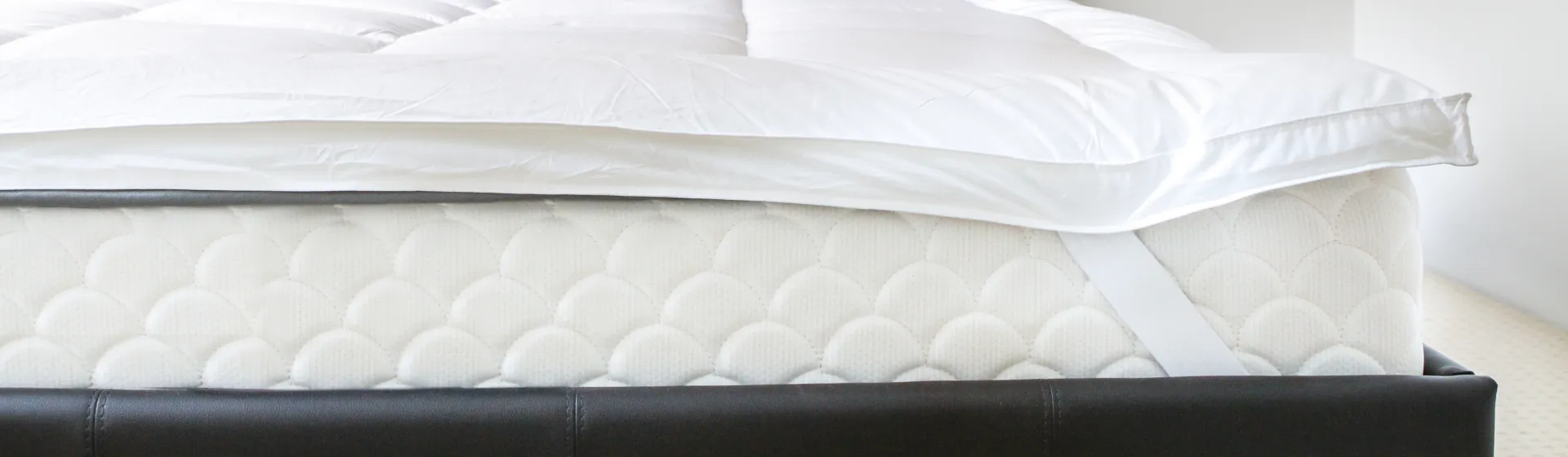 Pillow top branco colocado em colchão também branco encaixado em uma cama preta