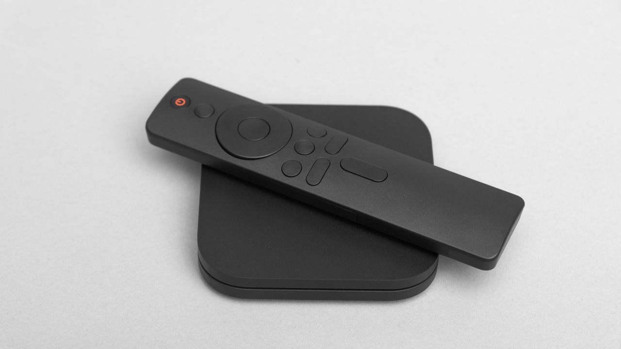 TV box com controle remoto em cima, tudo sobre superfície cinza.