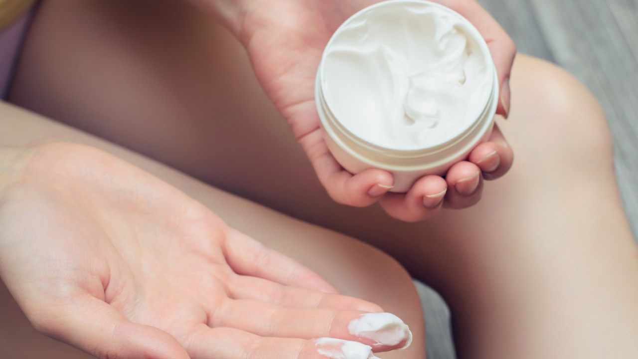 Creme para celulite em um pote redondo, segurado por uma mão feminina.