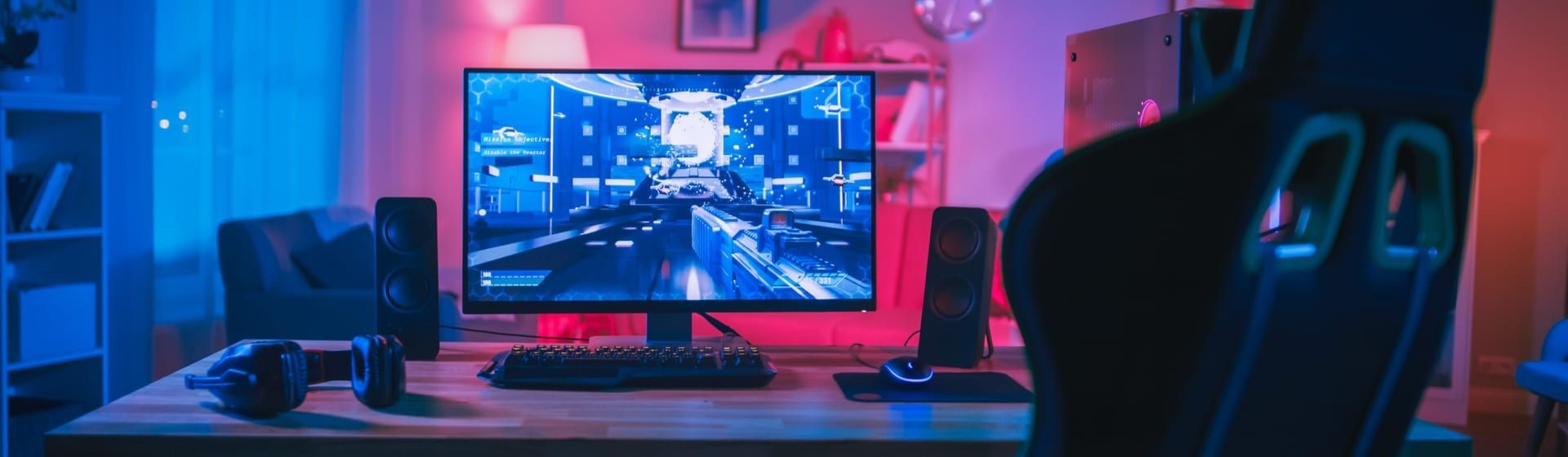 Monitor 1ms com teclado, caixas de som e fone de ouvido em cima de mesa de madeir
