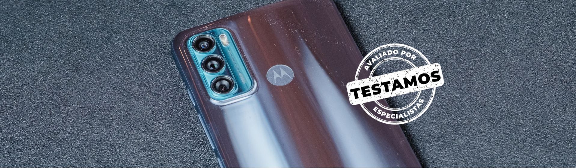 Parte superior do Moto G60 virado de costas, apoiado em um fundo cinza e com o selo do Testamos