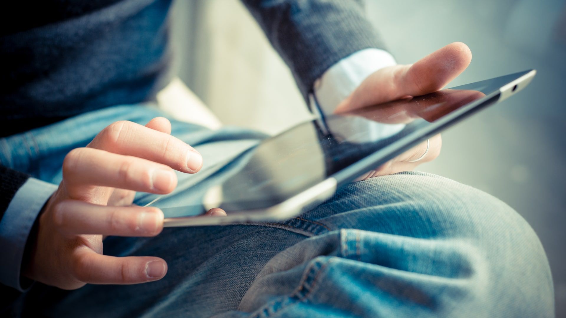 Homem segurando tablet com as duas mãos e apoiando na perna