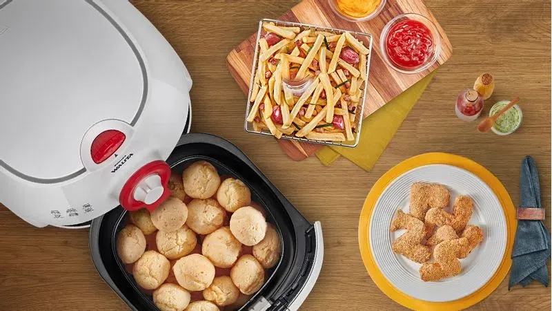 Air Fryer vista de cima com pães de queijo no cesto ao lado de pratos de batatas fritas e nuggets