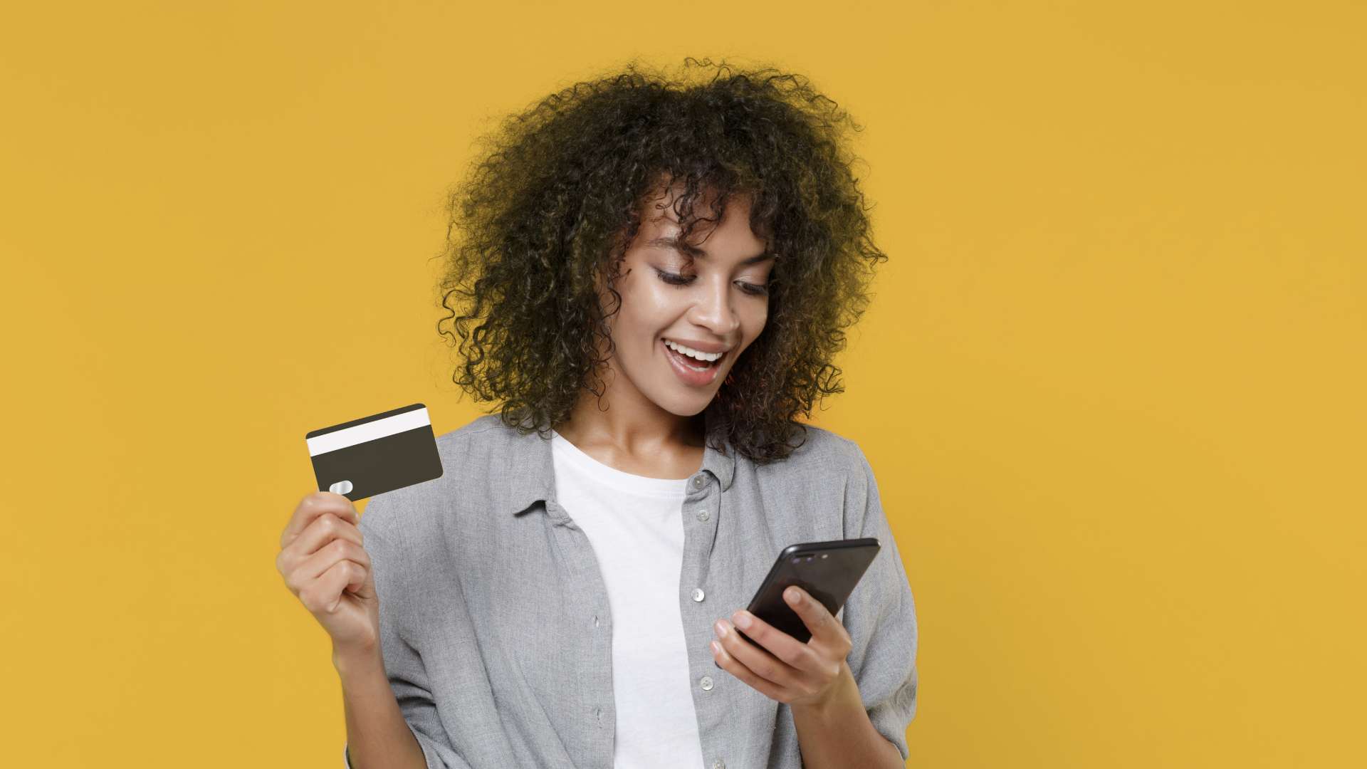 Mulher negra segurando celular com uma mão e cartão de crédito preto na outra
