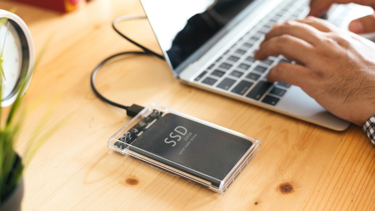 Homem utilizando SDD externo conectado ao notebook
