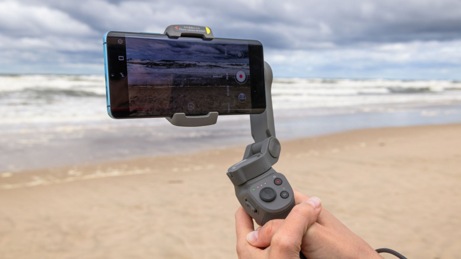 Pessoa segurando um estabilizador de celular em frente à praia
