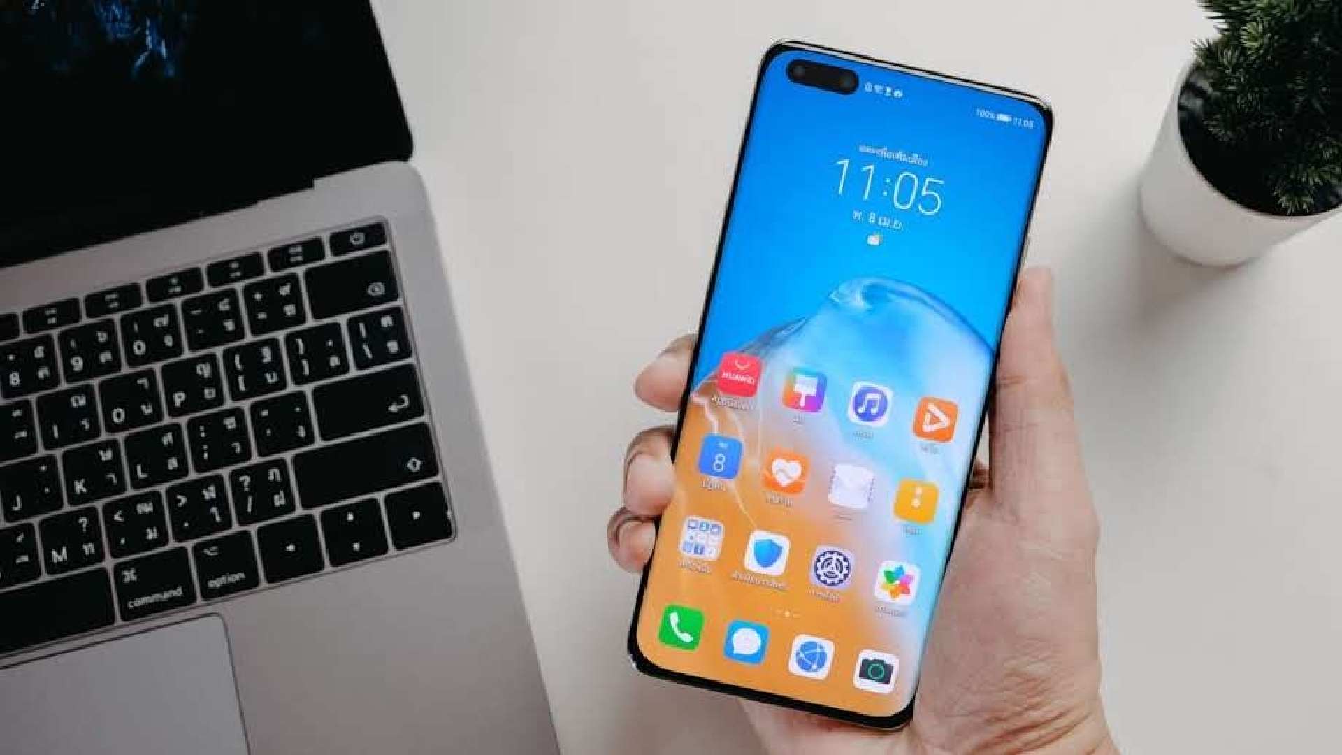 Huawei P40 Pro na mão de homem ao lado de notebook e vaso de plantas