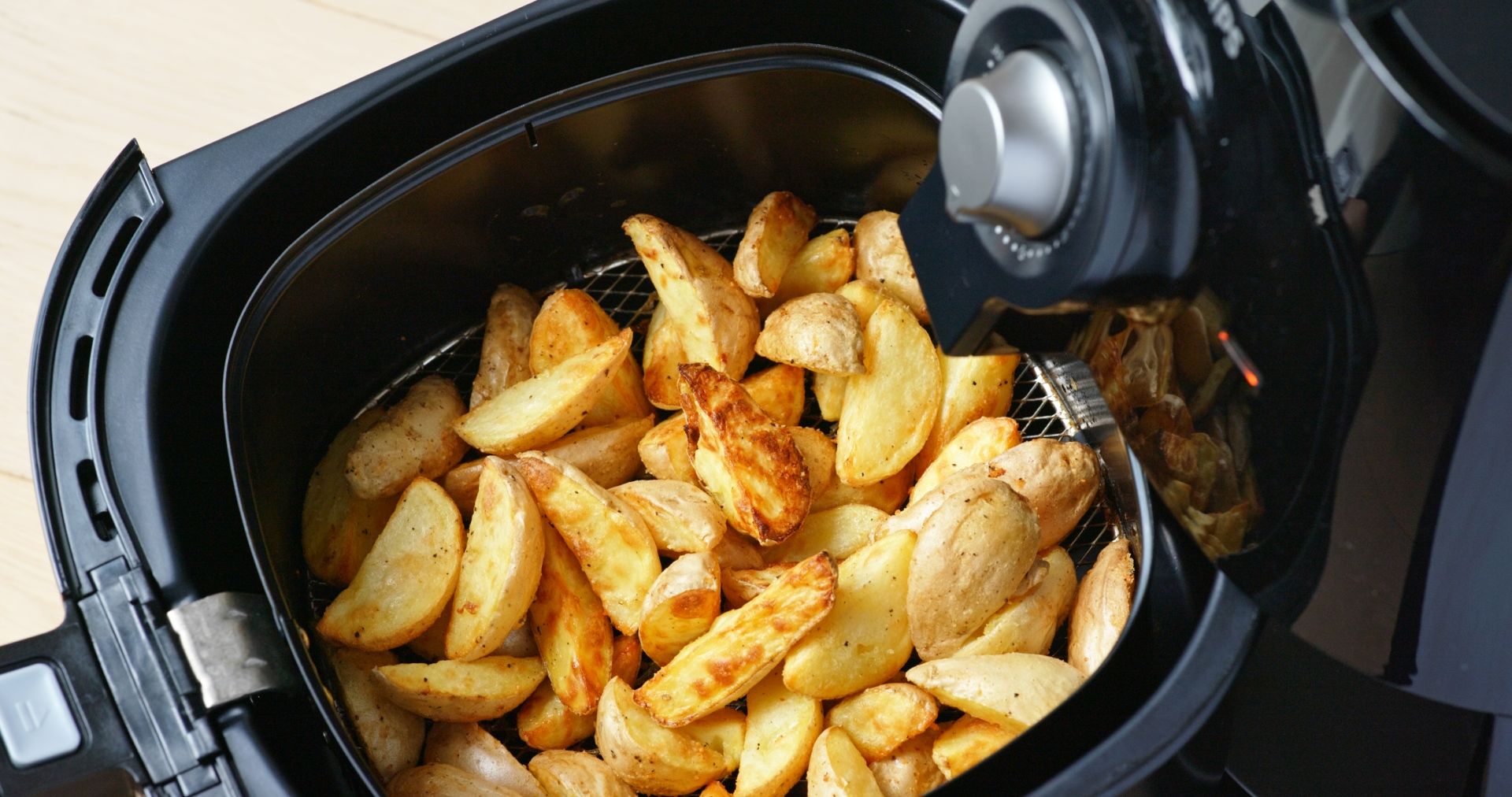 Cesto de airfryer aberto com batatas fritas cortadas em meia lua
