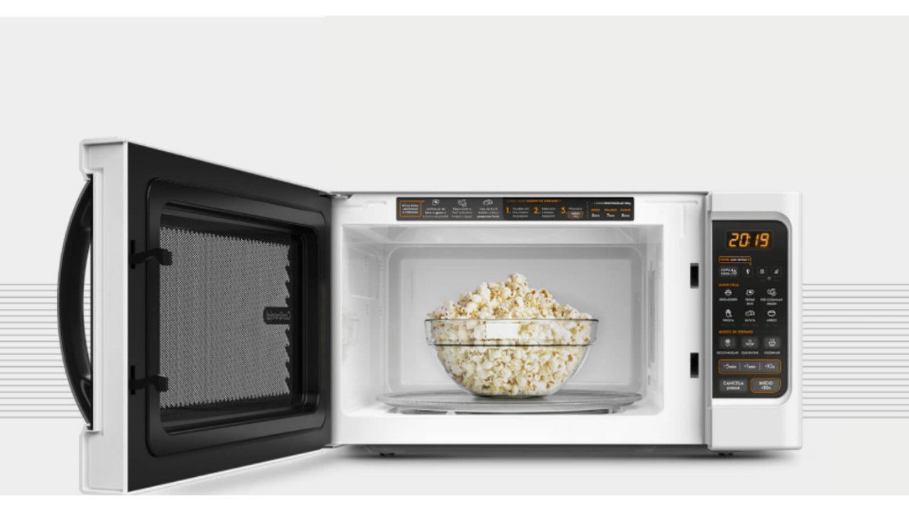 Micro-ondas Continental MC34B em fundo cinza com a porta aberta e um pote de pipoca no interior
