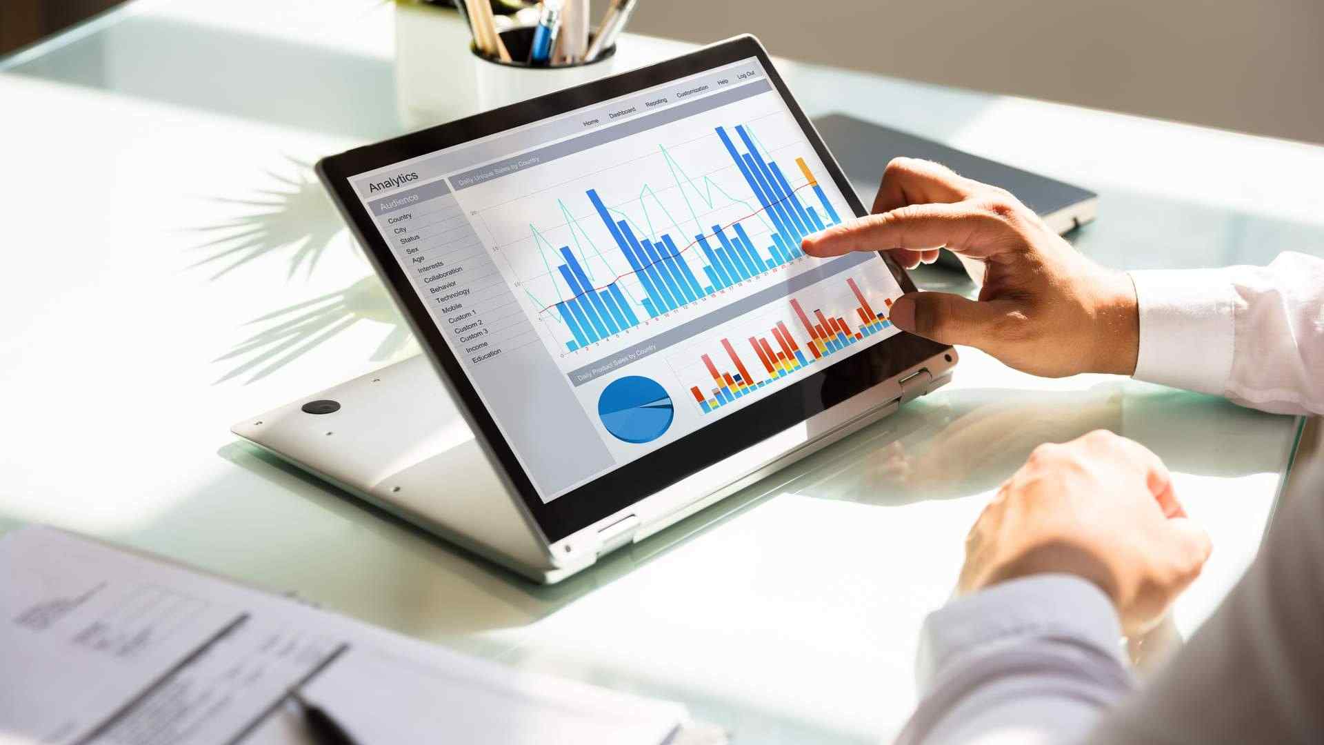 Homem observando gráficos empresariais em notebook 2 em 1 dobrado para trás