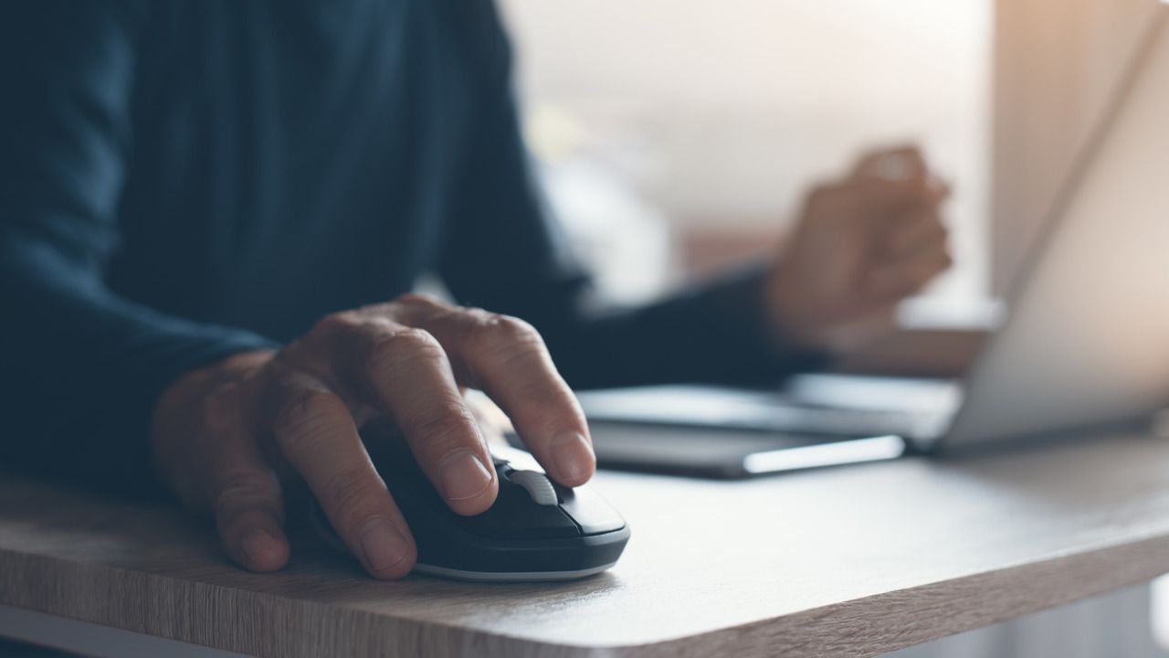 Homem usando mouse sem fio em uma mesa com um notebook
