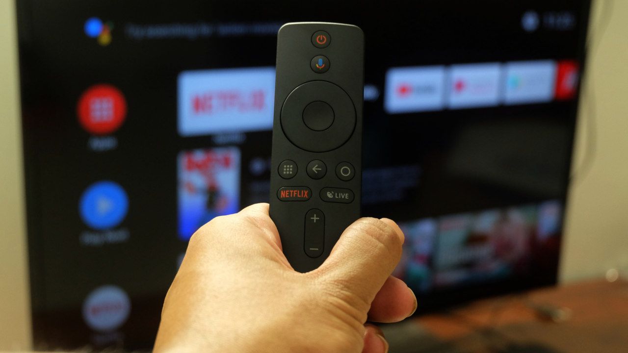 Controle remoto de uma TV box com tela de uma televisão aberta no menu de aplicativos ao fundo