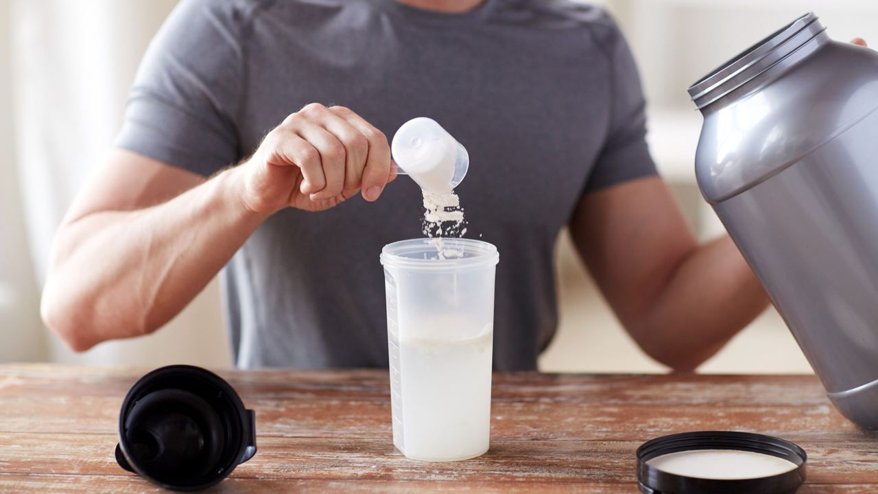 Homem adicionando glutamina ao shake em cima de mesa de madeira
