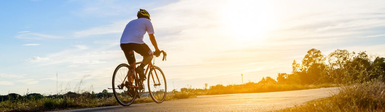 Homem pedalando bicicleta em direção ao pôr do sol