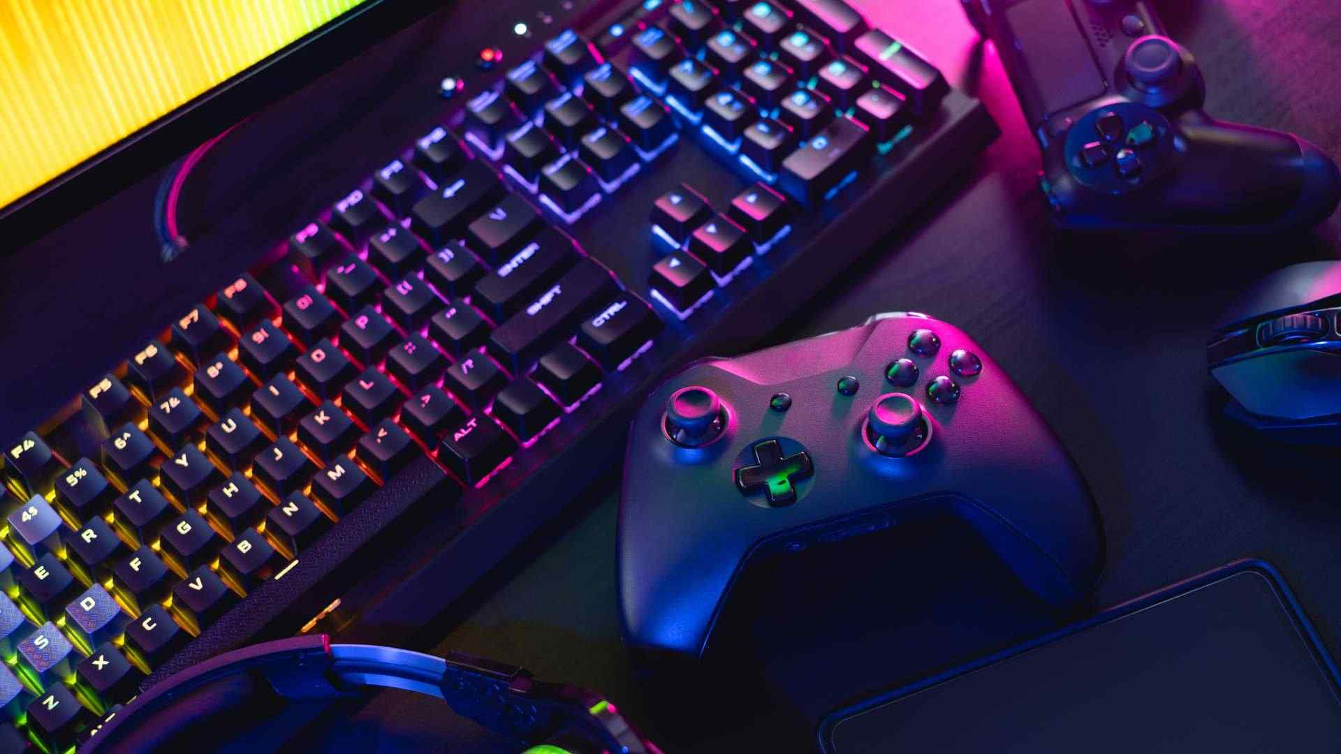 Mesa com itens gamer como teclado, headset, monitor, mouse e controles dispostos de forma desordenada
