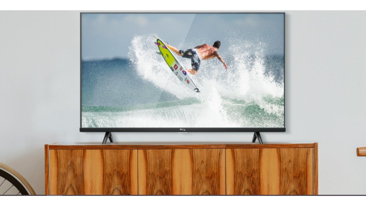 TV TCL S615 apoiada em rack de madeira clara com com tela mostrando um homem surfando
