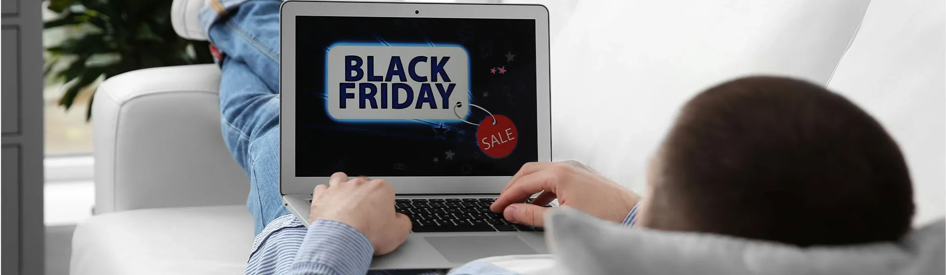 Homem deitado no sofá segurando um notebook com a tela mostrando "Black Friday"