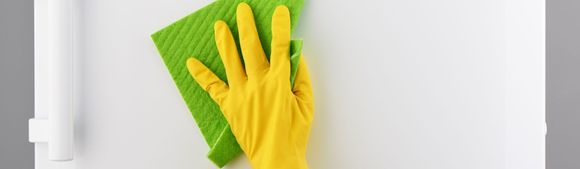 Pessoa usando luva amarela limpando uma geladeira branca com flanela verde
