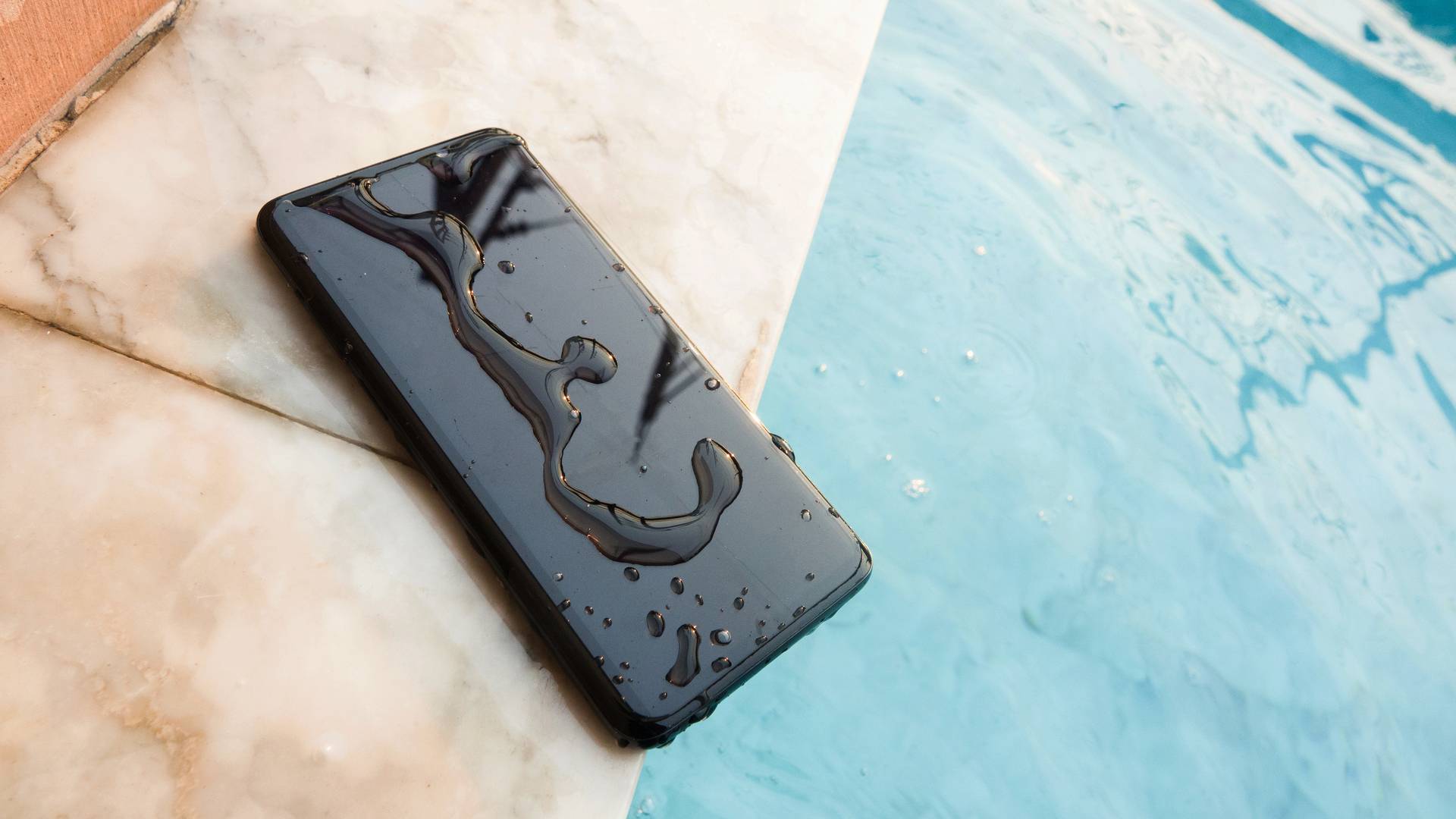 Celular preto molhado na borda de uma piscina