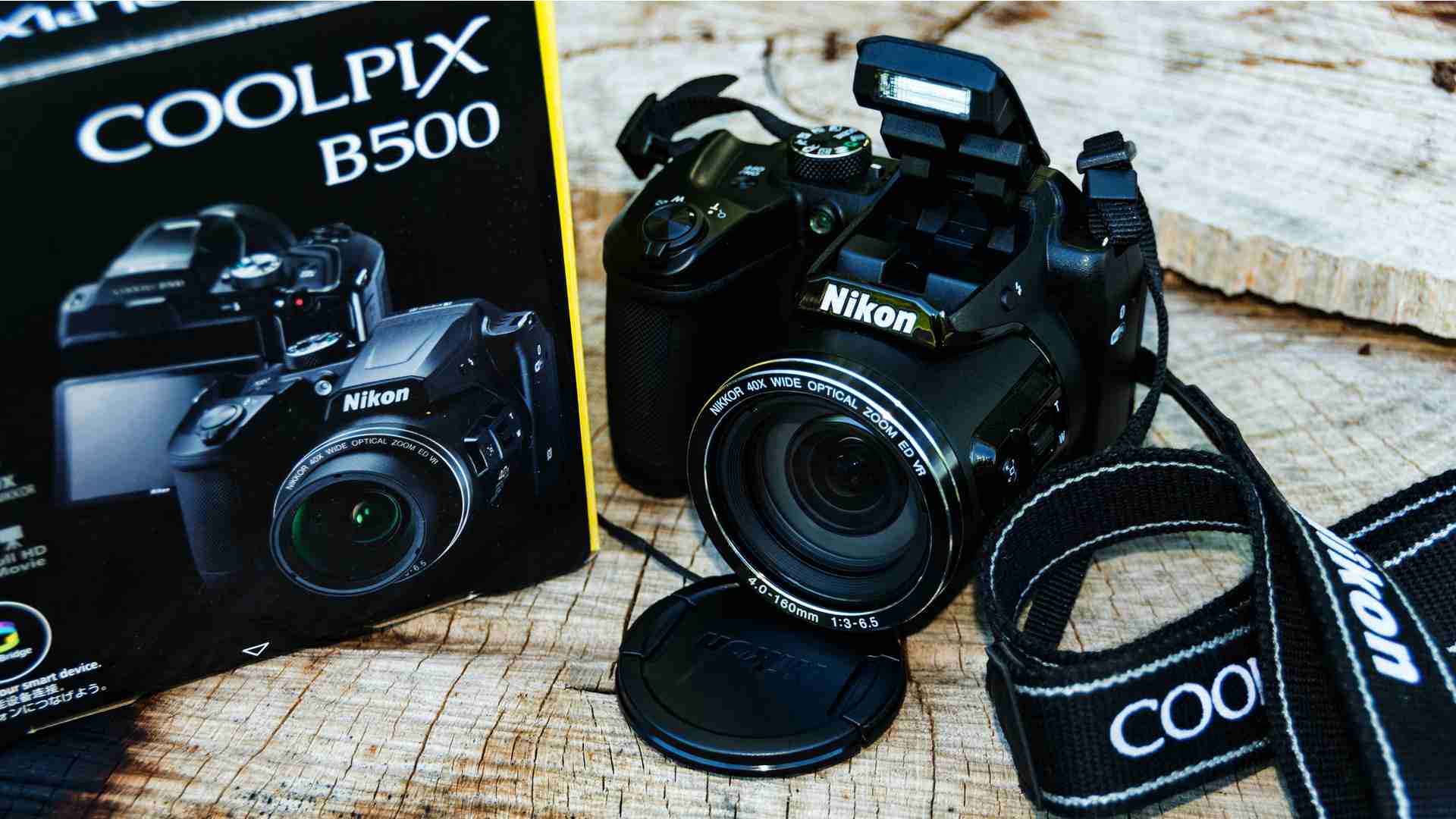 Máquina fotográfica semiprofissional Nikon B500 ao lado de sua caixa apoiada em mesa de madeira