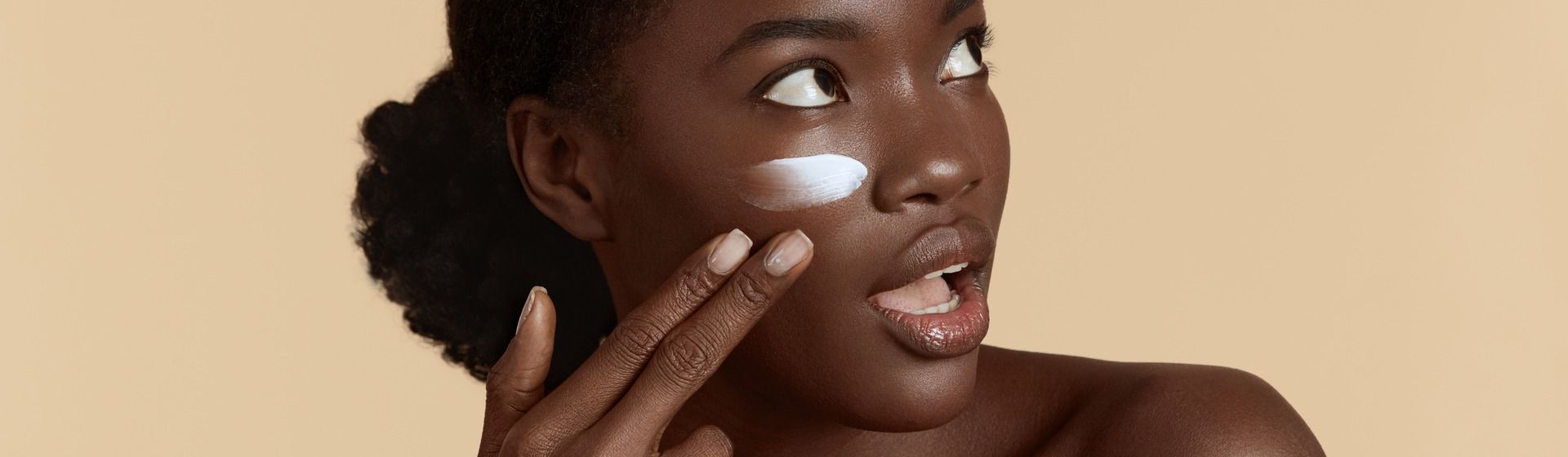 Mulher negra aplicando hidratante facial no rosto