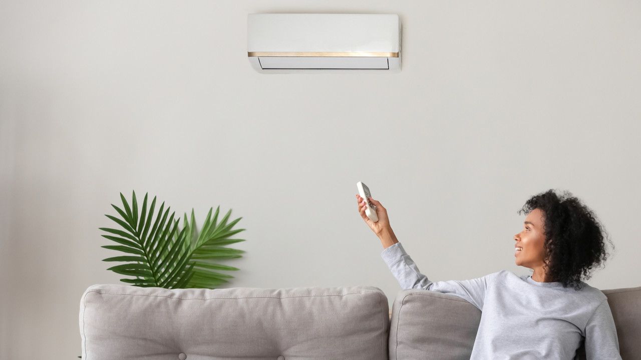 Mulher de cabelo cacheado apontando controle remoto para um ar-condicionado split branco instalado em parede